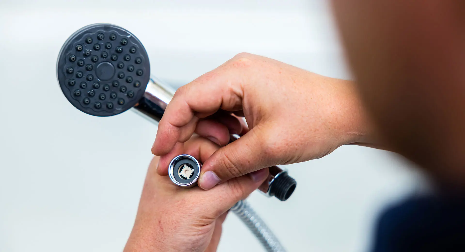 A close-up of a person holding a shower head and hose attachment