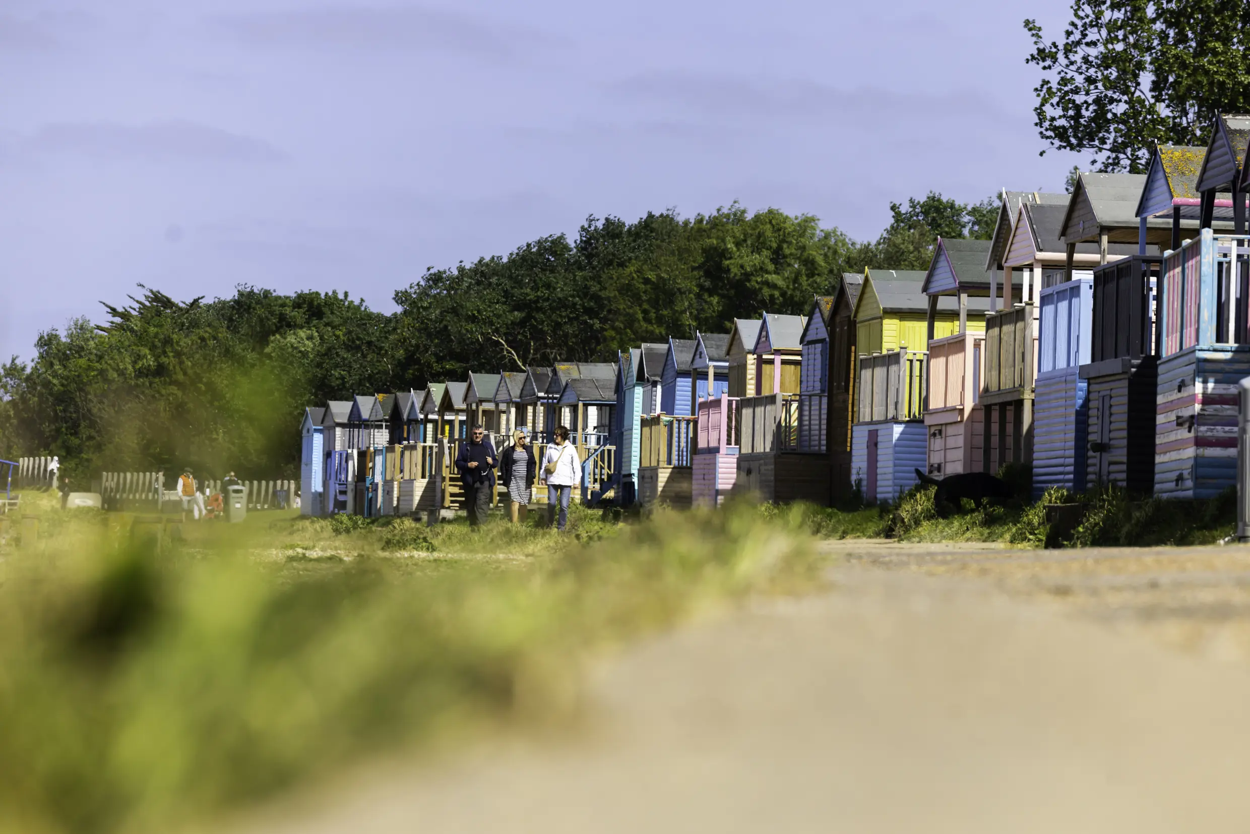 Three people walk beside beach huts on Swalecliffe Beach